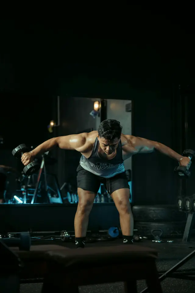Athlete performing a dumbbell movement in a dark gym